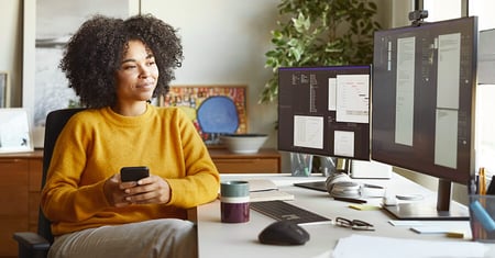 woman holding her phone while looking at computer screen
