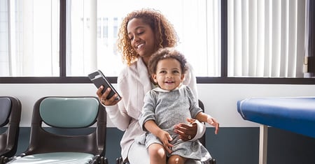 woman holding baby looking at phone in hospital waiting room 
