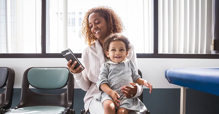 woman holding baby looking at phone in hospital waiting room 
