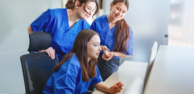 three women wearing scrubs looking at computer